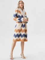 Femme blonde tenant une tasse, robe de chambre polaire mi-longue zigzag bleu ardoise et caramel, col châle crème, sandales plates blanches à lanières