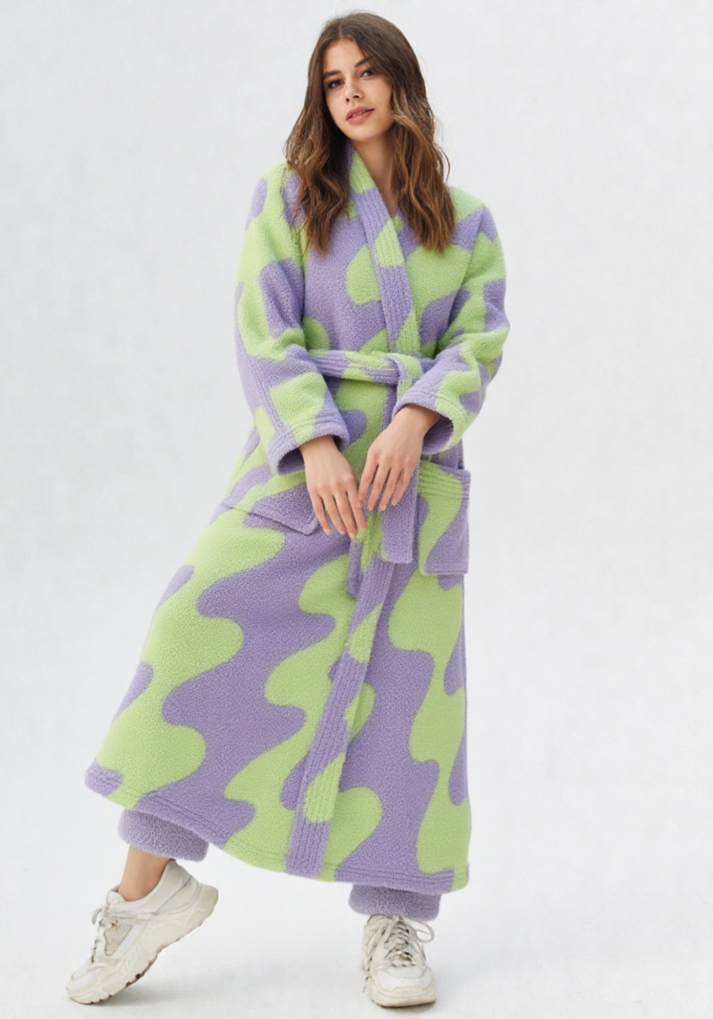 Femme portant une robe de chambre polaire longue à motifs abstraits lilas et vert anis, ceinture lilas, baskets blanches, mains croisées