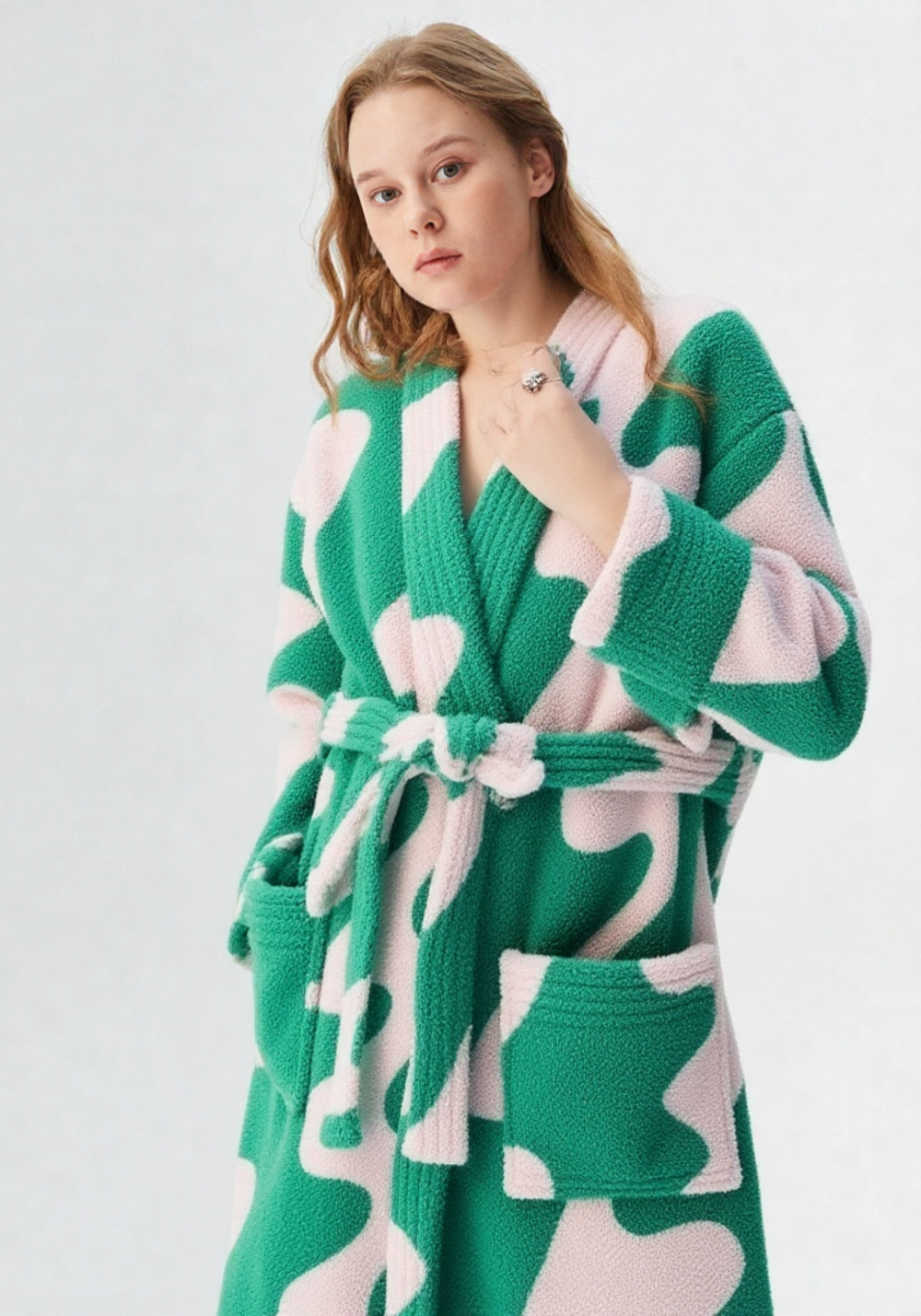 Gros plan buste femme en robe de chambre polaire verte et rose à motifs abstraits, col V et grandes poches, collier délicat visible