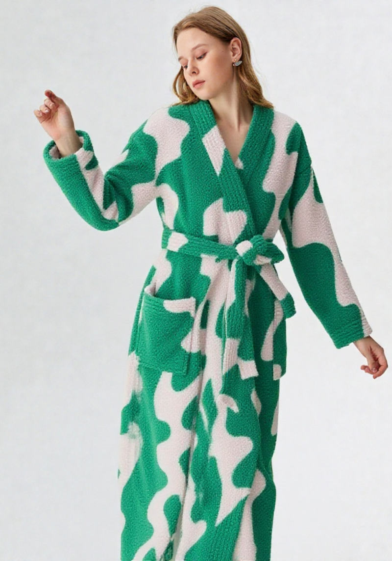 Femme portant une robe de chambre longue polaire blanche à motifs verts abstraits, col V croisé sans capuche, ceinture verte et poche plaquée