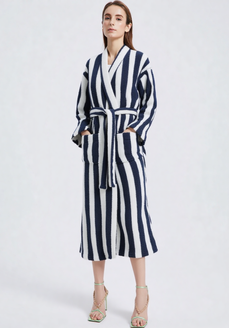 Femme de face portant une robe de chambre longue polaire à rayures verticales bleu marine et blanc, col V, ceinture blanche, sandales à talons vert fluo