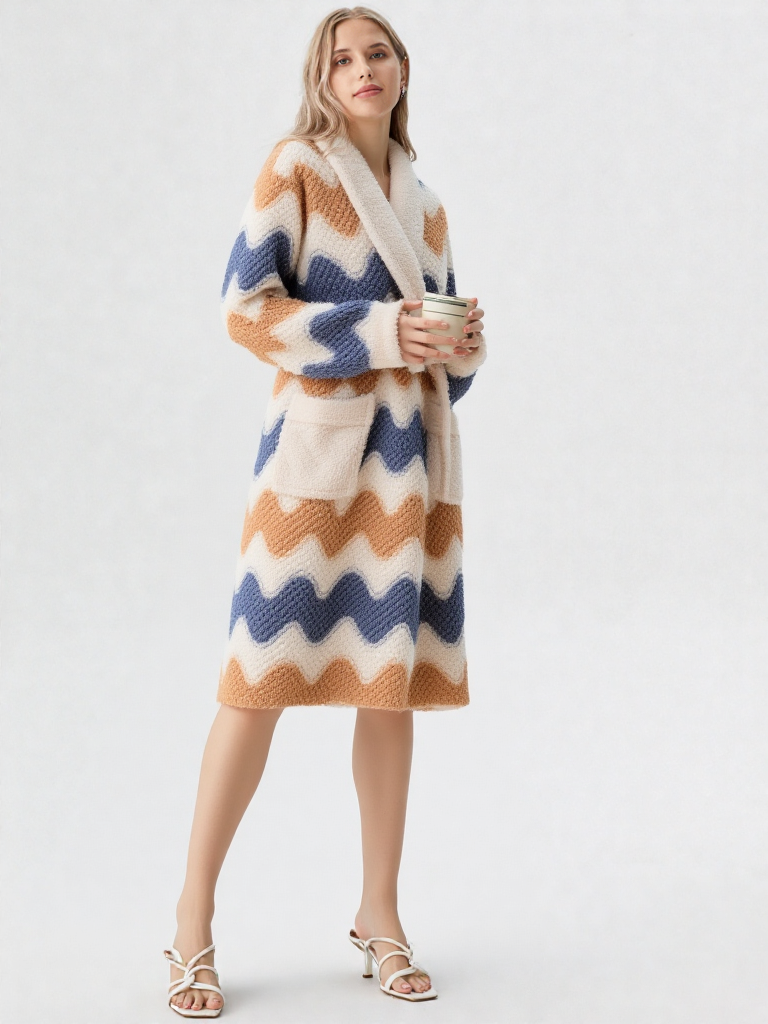 Femme blonde tenant une tasse, robe de chambre polaire mi-longue zigzag bleu ardoise et caramel, col châle crème, sandales plates blanches à lanières